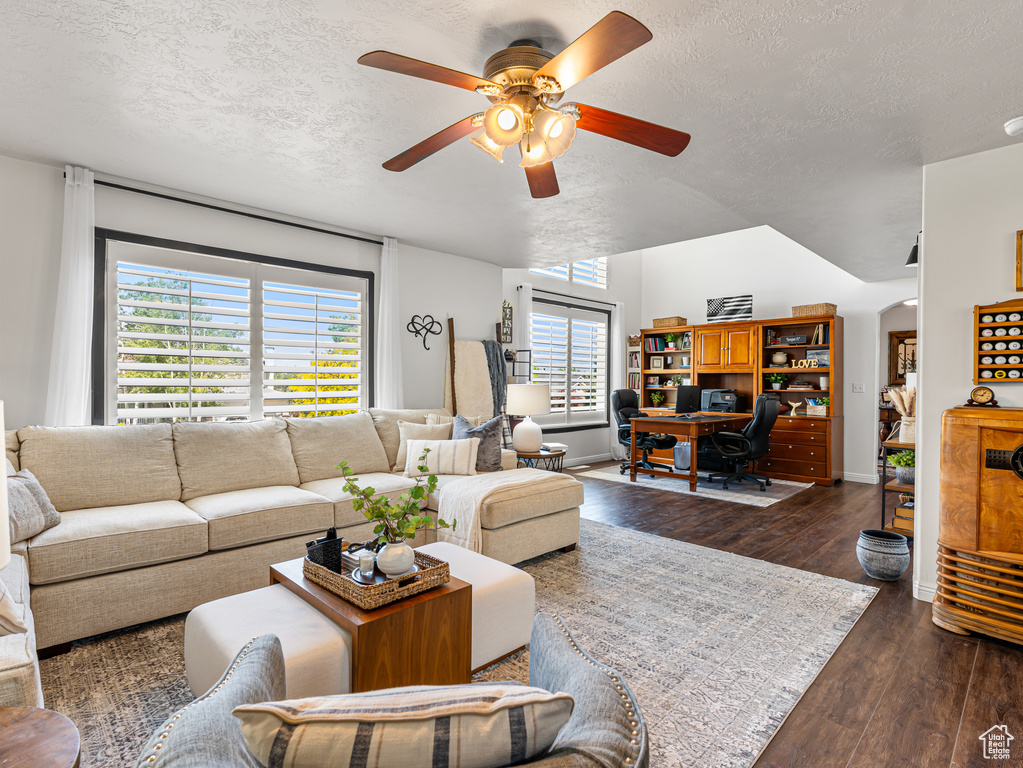 Living area with a textured ceiling, ceiling fan, dark wood-type flooring, a desk, and baseboards
