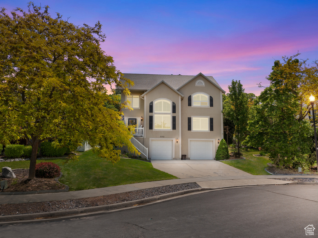Traditional-style house featuring concrete driveway, stucco siding, a yard, a garage, and stairway