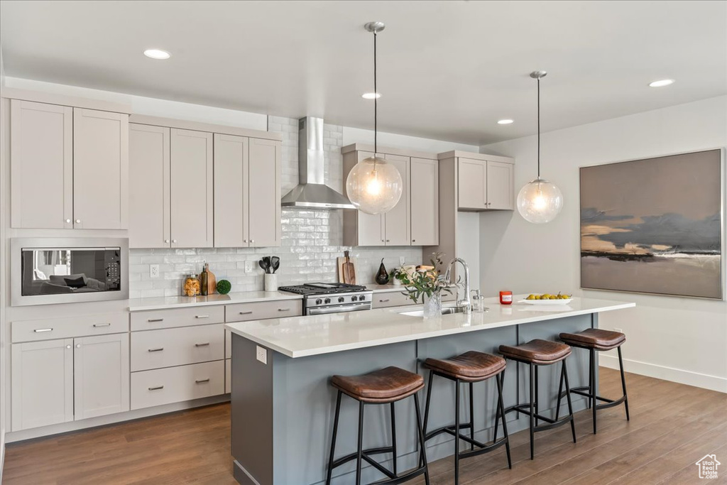 Kitchen featuring wall chimney exhaust hood, a sink, built in microwave, stainless steel range with gas cooktop, and wood finished floors