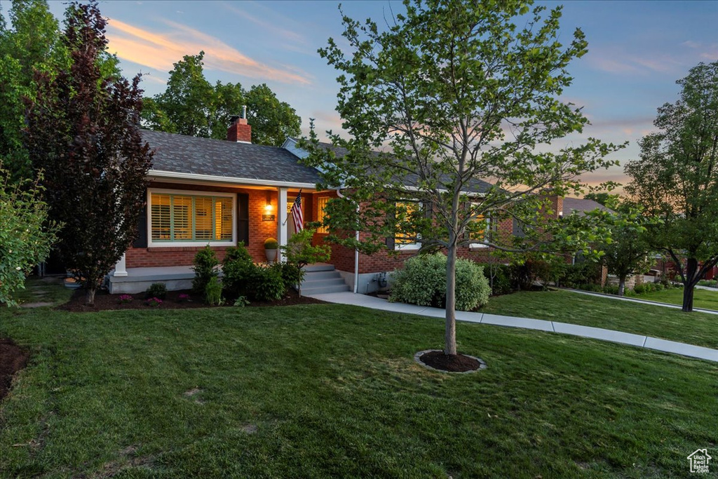 View of front of property featuring brick siding, a yard, and a chimney