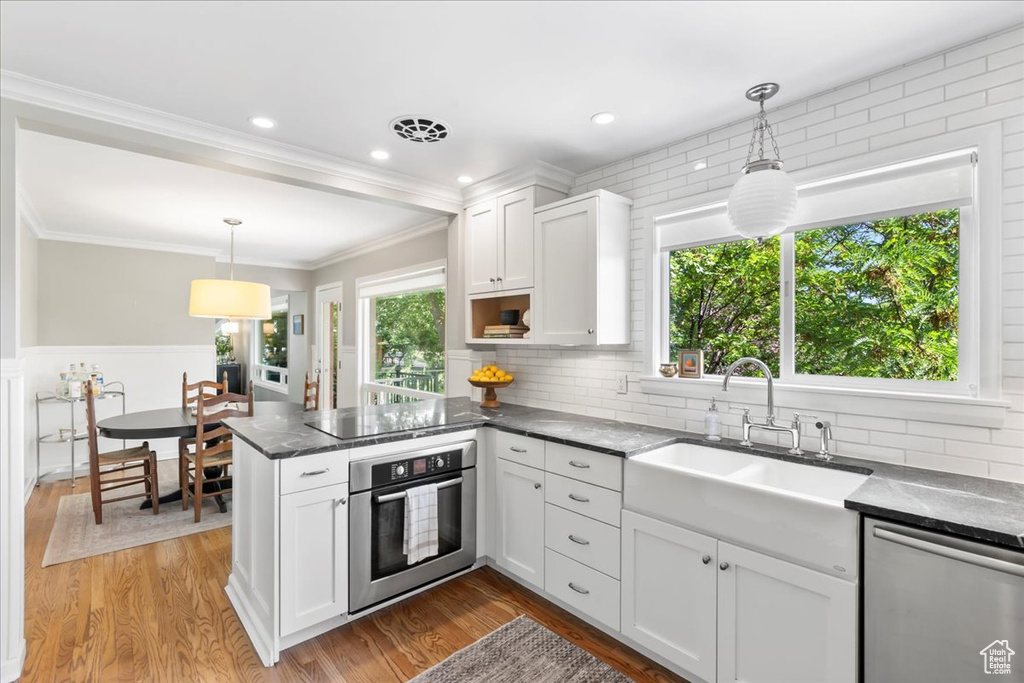 Kitchen featuring stainless steel appliances, a sink, a peninsula, white cabinets, and ornamental molding