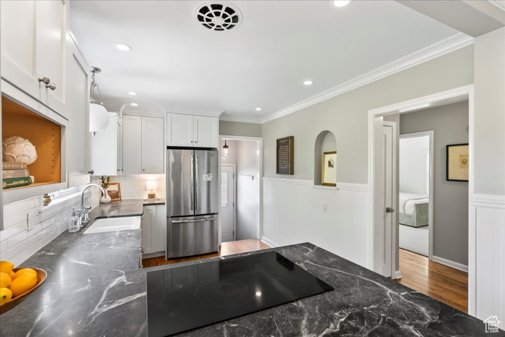 Kitchen featuring freestanding refrigerator, a sink, black electric stovetop, ornamental molding, and white cabinets