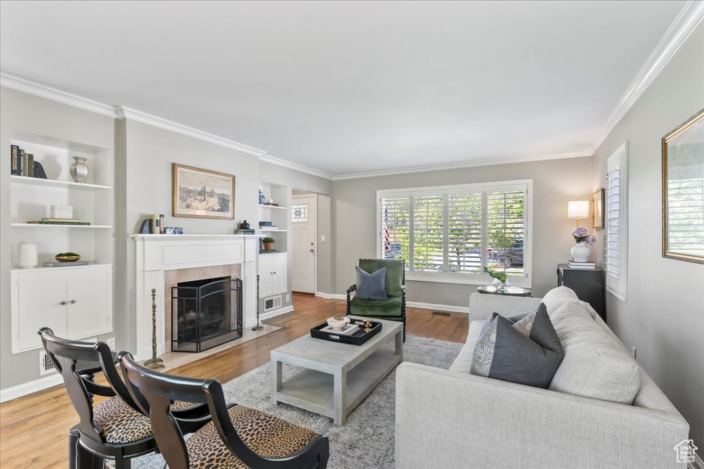 Living room featuring a fireplace, ornamental molding, wood finished floors, built in shelves, and baseboards
