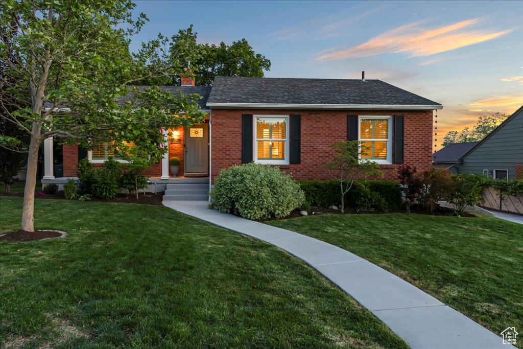 View of front of home featuring brick siding, a lawn, and a chimney