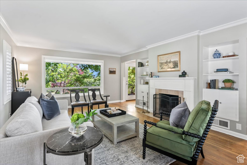 Living area with built in shelves, crown molding, a fireplace, wood finished floors, and baseboards