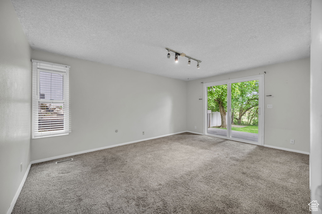 Carpeted spare room featuring rail lighting, a textured ceiling, and baseboards