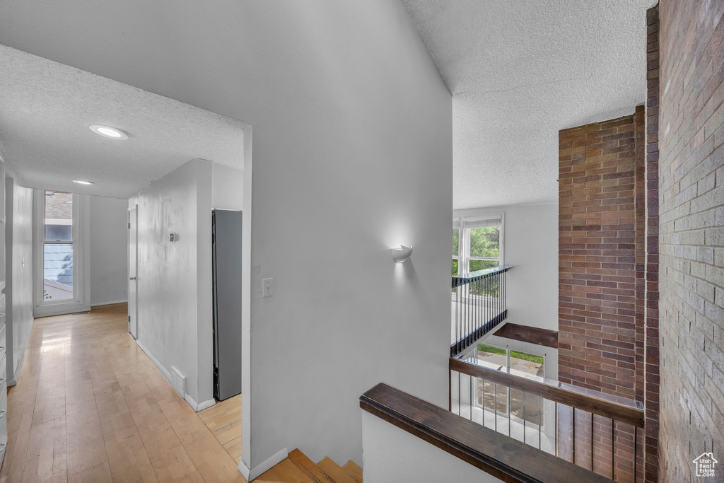 Hall featuring a textured ceiling, light wood finished floors, and baseboards