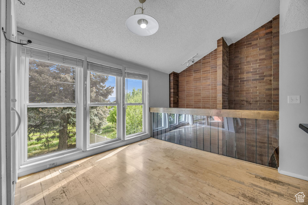 Empty room featuring vaulted ceiling, a textured ceiling, and wood-type flooring
