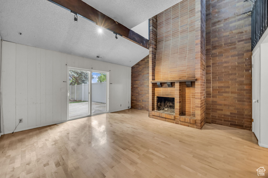 Unfurnished living room with wood finished floors, rail lighting, a fireplace, a textured ceiling, and lofted ceiling