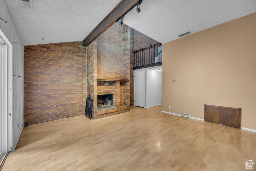 Unfurnished living room featuring a fireplace, wood finished floors, high vaulted ceiling, a textured ceiling, and baseboards