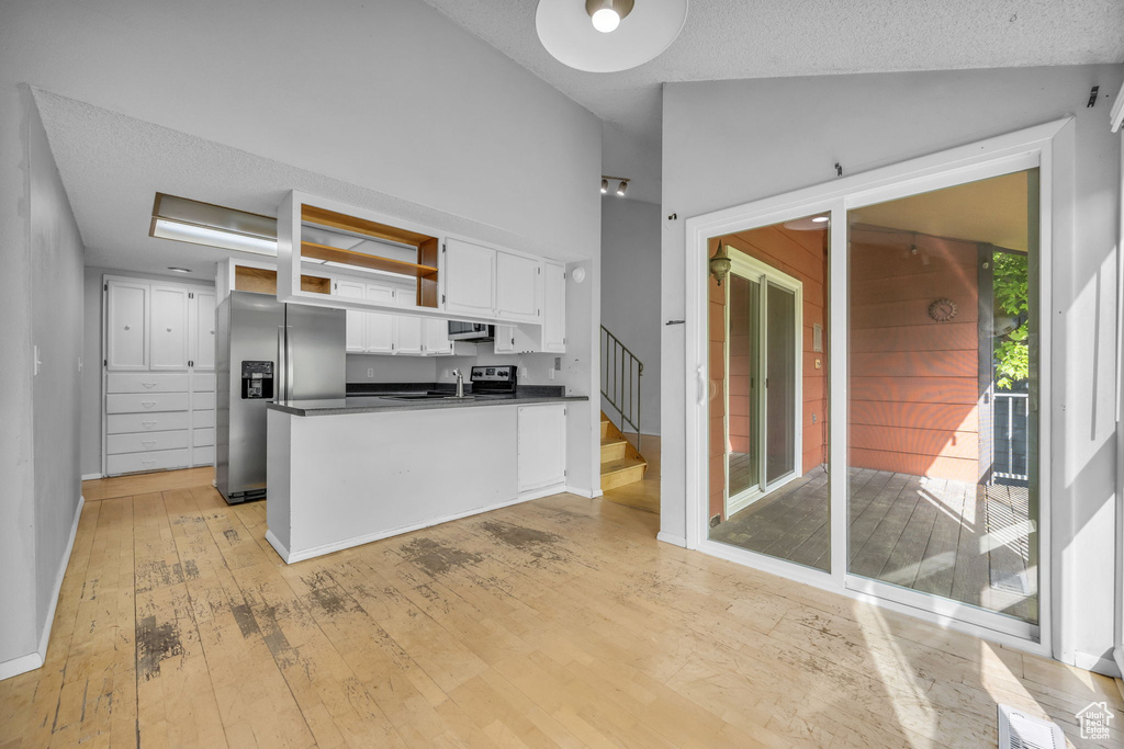 Kitchen with stainless steel refrigerator with ice dispenser, dark countertops, white cabinetry, light wood finished floors, and vaulted ceiling