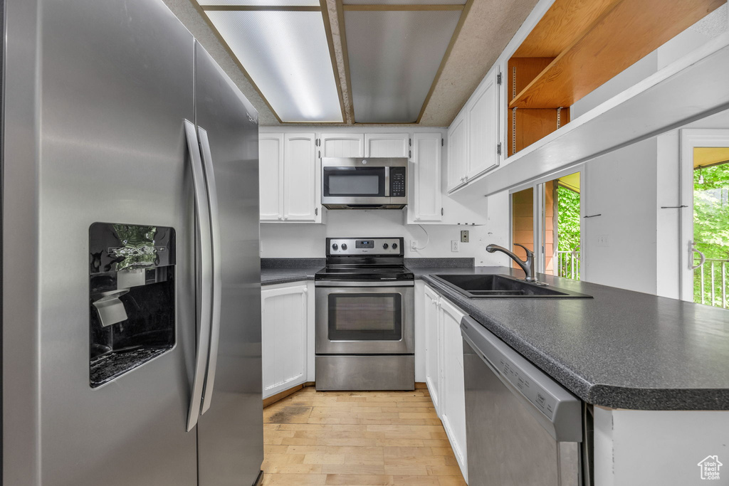 Kitchen with stainless steel appliances, a sink, dark countertops, light wood-style floors, and white cabinets