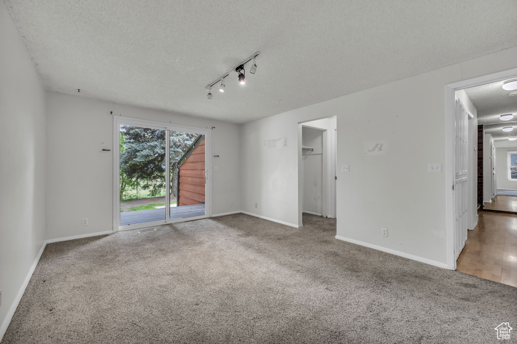 Carpeted spare room with a textured ceiling, track lighting, and baseboards