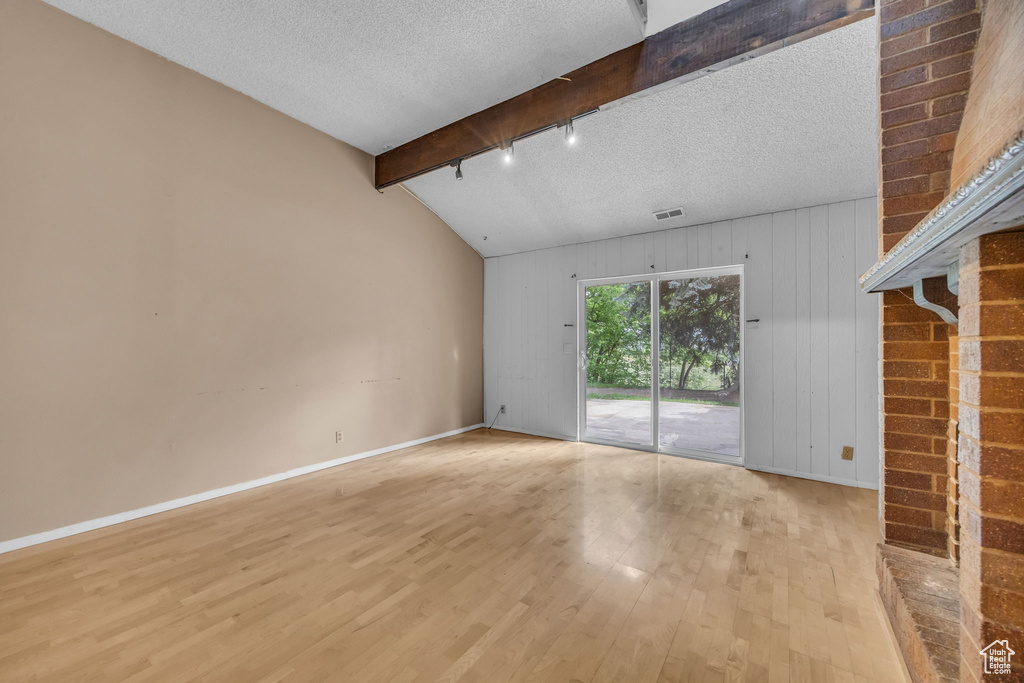 Unfurnished living room featuring light wood-type flooring, baseboards, a textured ceiling, wooden walls, and track lighting