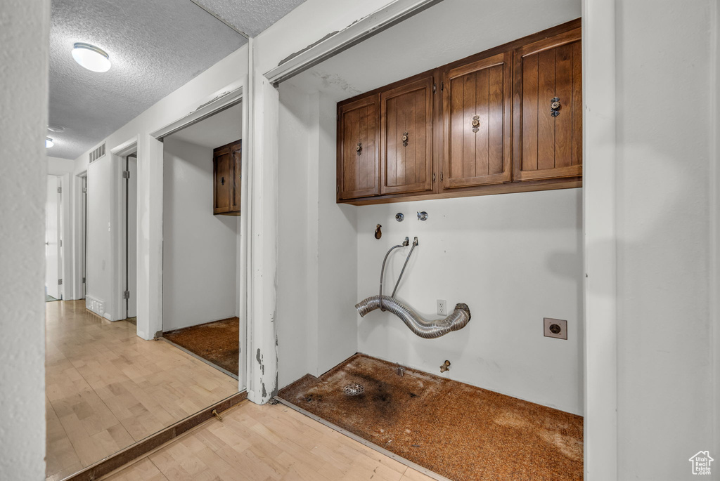 Washroom with cabinet space, hookup for a gas dryer, light wood finished floors, a textured ceiling, and hookup for an electric dryer