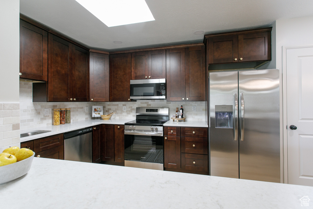 Kitchen featuring appliances with stainless steel finishes, light countertops, decorative backsplash, and dark brown cabinets