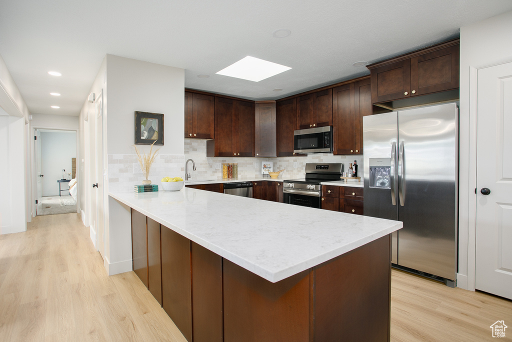 Kitchen featuring stainless steel appliances, a peninsula, light wood-style flooring, a skylight, and dark brown cabinets