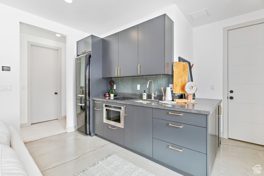Kitchen with gray cabinetry, a sink, stainless steel oven, freestanding refrigerator, and backsplash