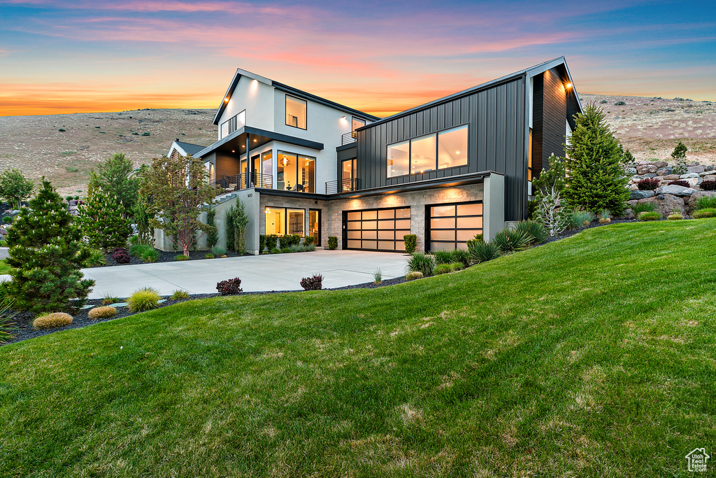 Rear view of property with an attached garage, a lawn, driveway, and a balcony