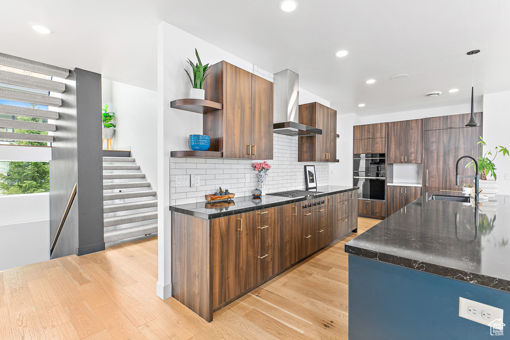 Kitchen featuring wall chimney range hood, open shelves, double wall oven, modern cabinets, and a sink