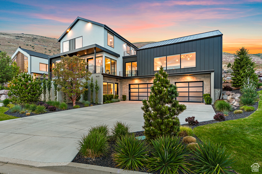 Contemporary home with a balcony, a standing seam roof, a garage, driveway, and board and batten siding