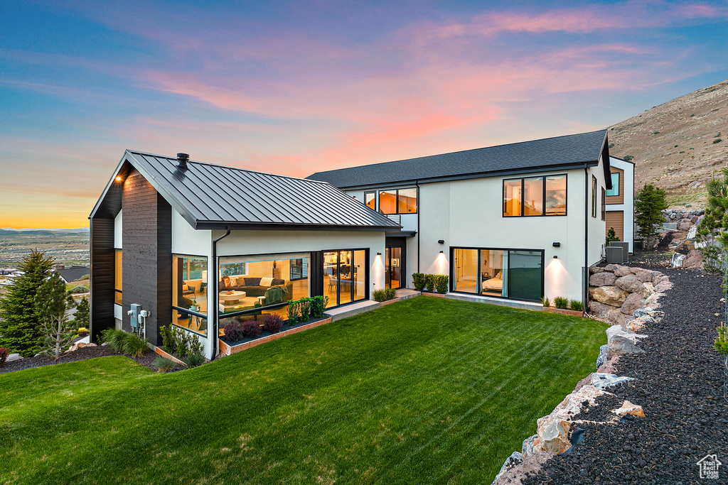 Back of property at dusk featuring a standing seam roof, stucco siding, and a yard
