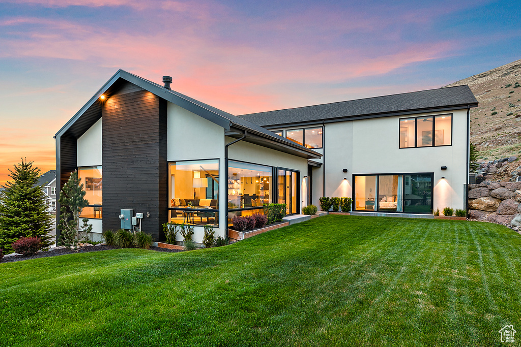 Back of property at dusk with a yard, a sunroom, and stucco siding