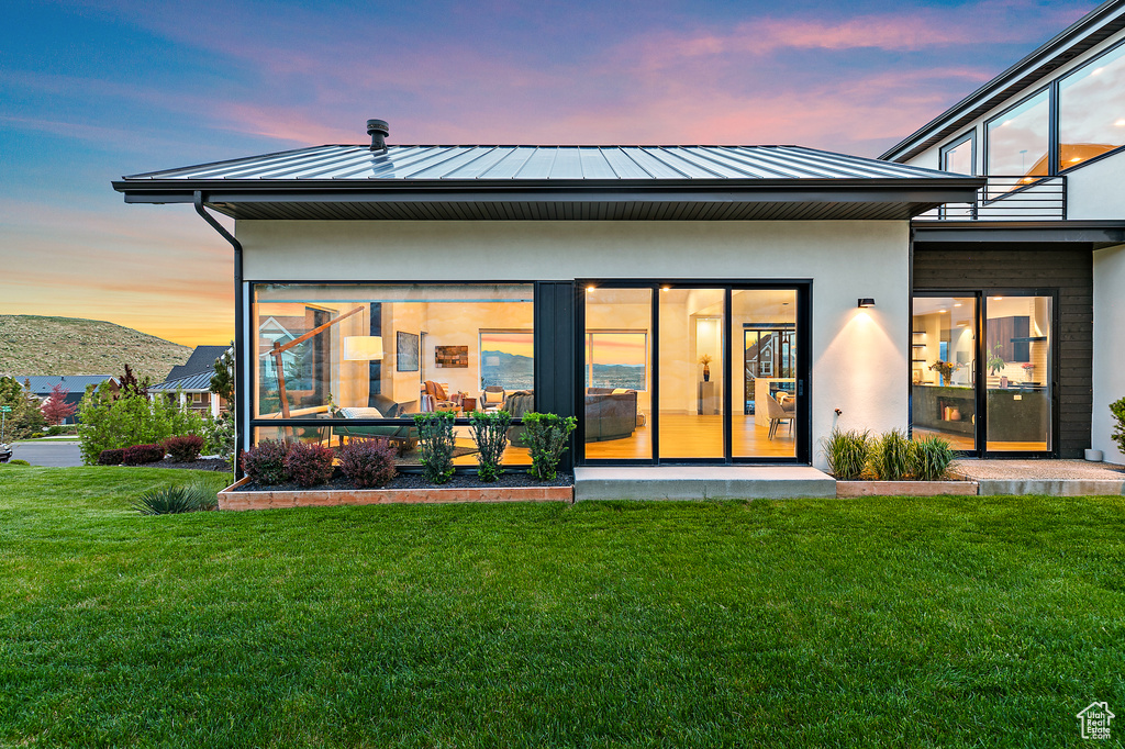 Back of house at dusk featuring a standing seam roof, a yard, metal roof, and stucco siding