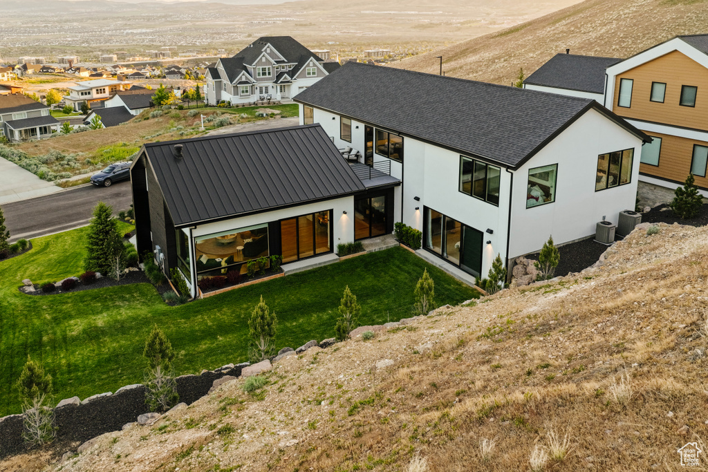 Rear view of property featuring stucco siding, a residential view, metal roof, a yard, and cooling unit