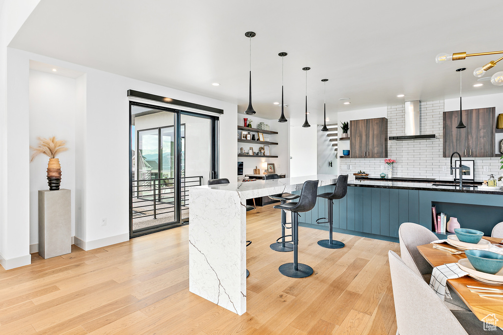 Kitchen with wall chimney range hood, a sink, modern cabinets, open shelves, and light wood finished floors