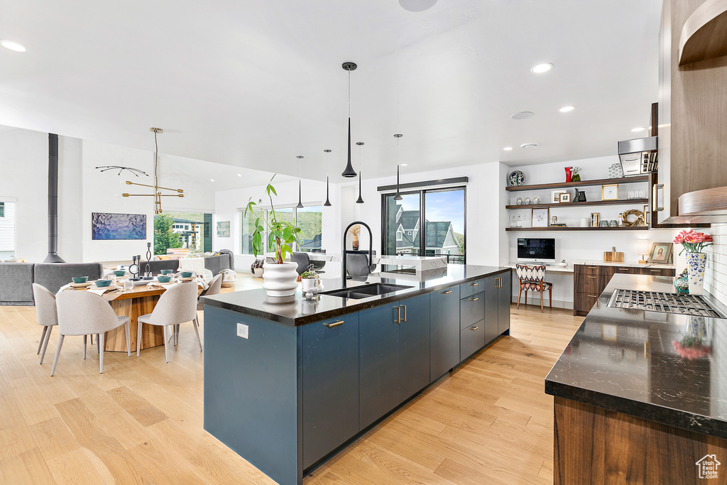 Kitchen featuring a sink, open floor plan, open shelves, light wood-style flooring, and dark countertops