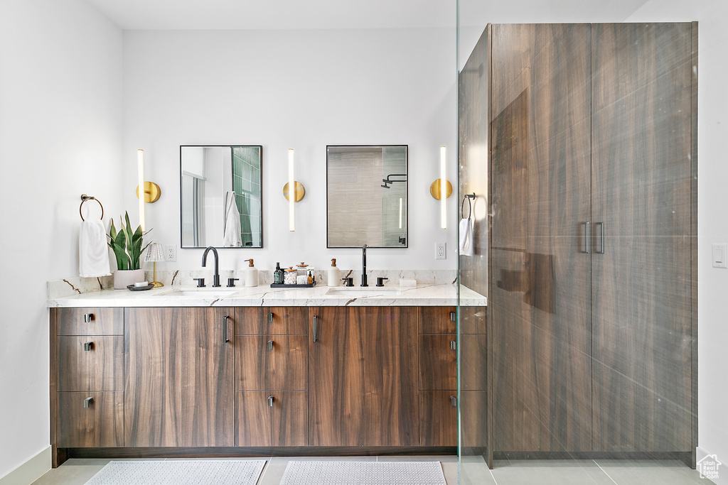 Full bath featuring a stall shower, double vanity, and baseboards