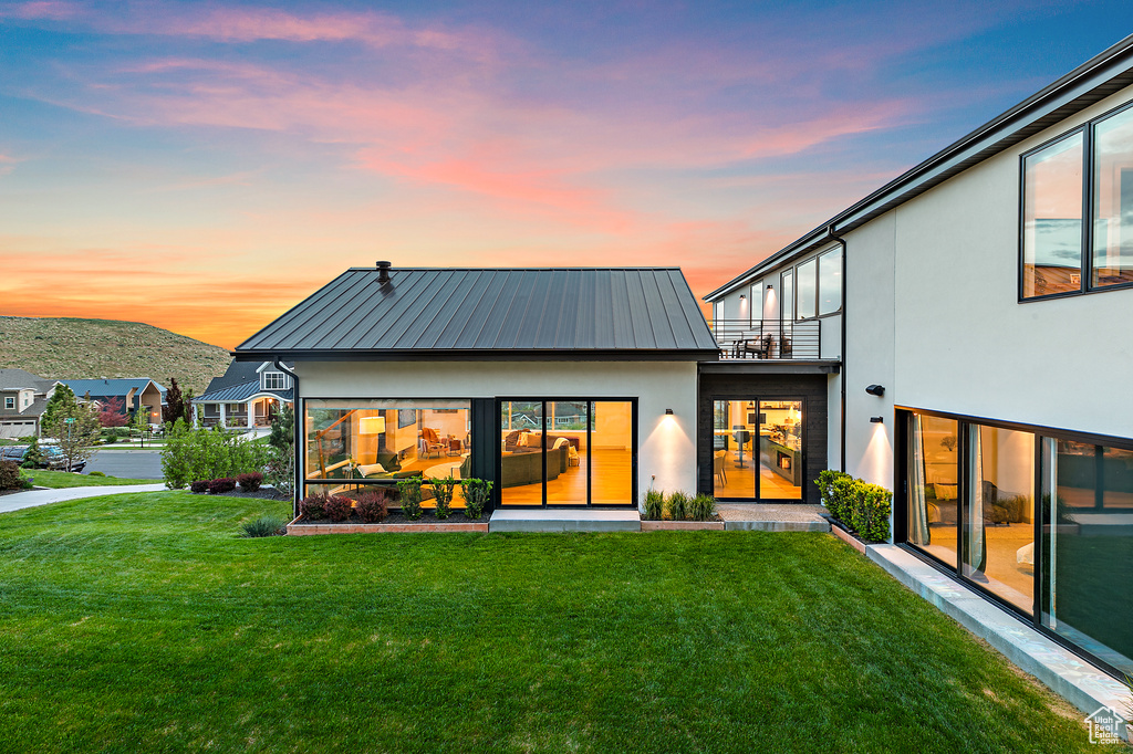 Rear view of property featuring a balcony, stucco siding, a lawn, and metal roof