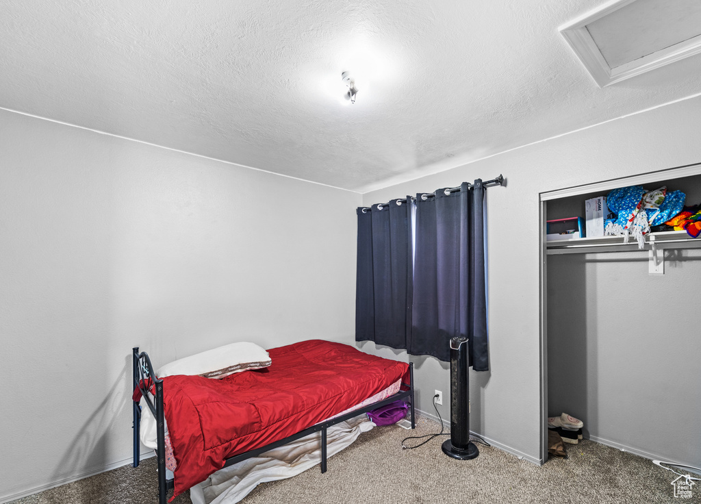 Bedroom featuring a textured ceiling, attic access, baseboards, carpet, and a closet