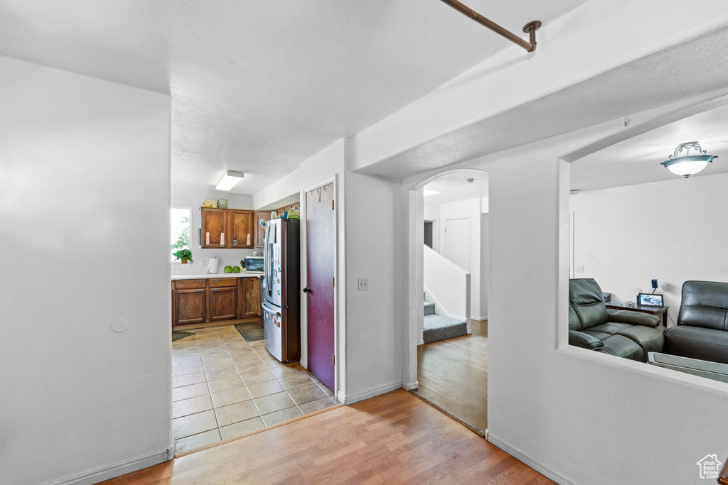 Kitchen with freestanding refrigerator, arched walkways, light wood-style floors, light countertops, and brown cabinets