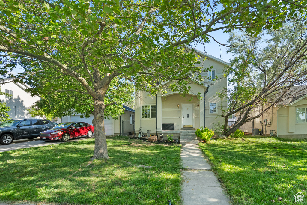 View of property hidden behind natural elements featuring a front lawn, a garage, central AC, and stucco siding