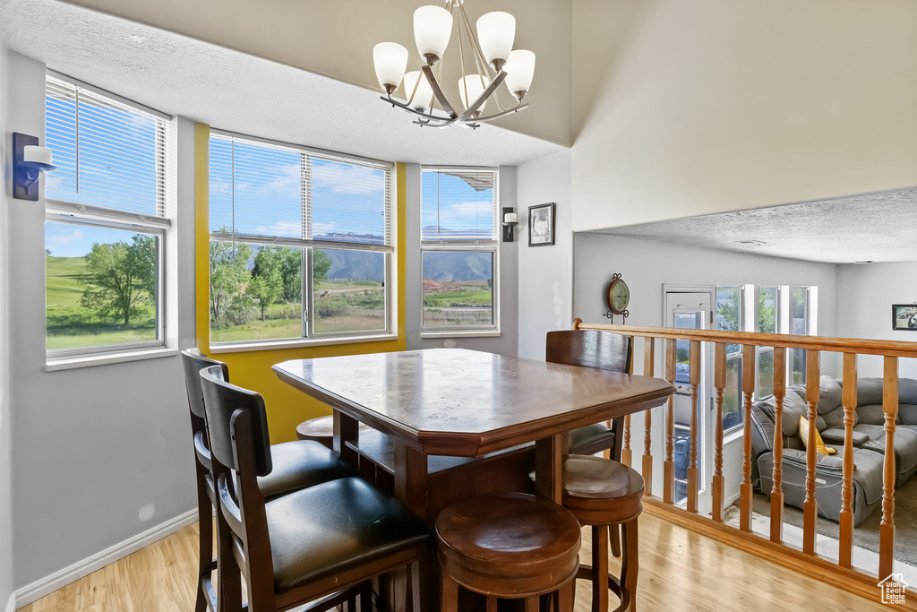 Dining space featuring light wood finished floors, a chandelier, baseboards, and a textured ceiling