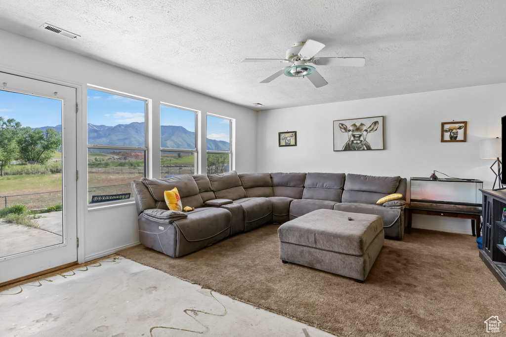 Living room featuring a mountain view, a textured ceiling, carpet floors, and a ceiling fan