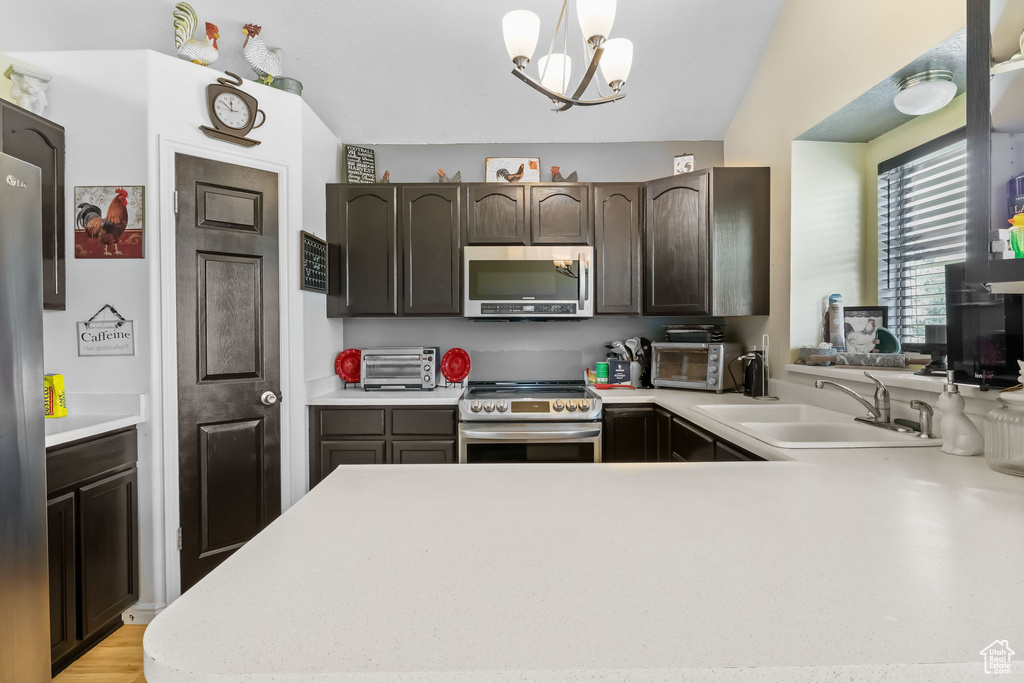 Kitchen featuring appliances with stainless steel finishes, a sink, light countertops, dark brown cabinets, and a peninsula