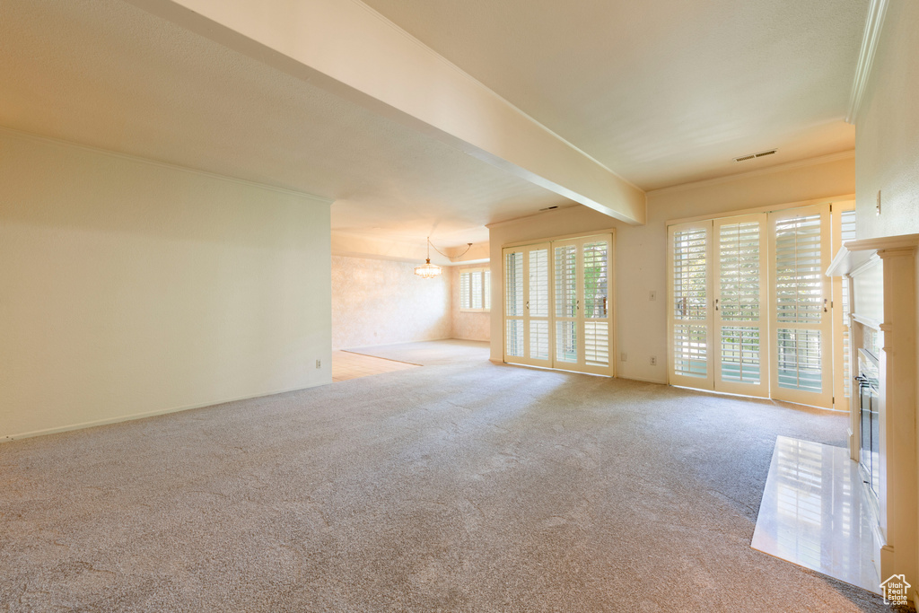 Unfurnished room featuring carpet flooring, beamed ceiling, a fireplace with raised hearth, and a chandelier