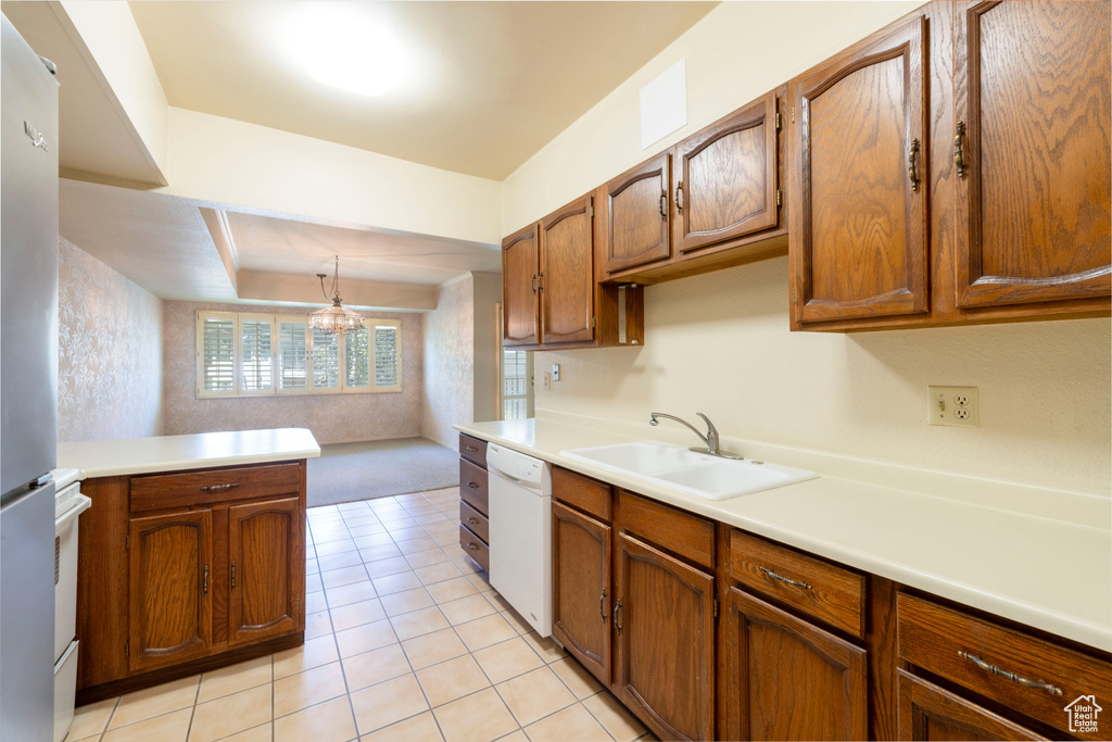 Kitchen with dishwasher, a sink, light countertops, brown cabinets, and freestanding refrigerator