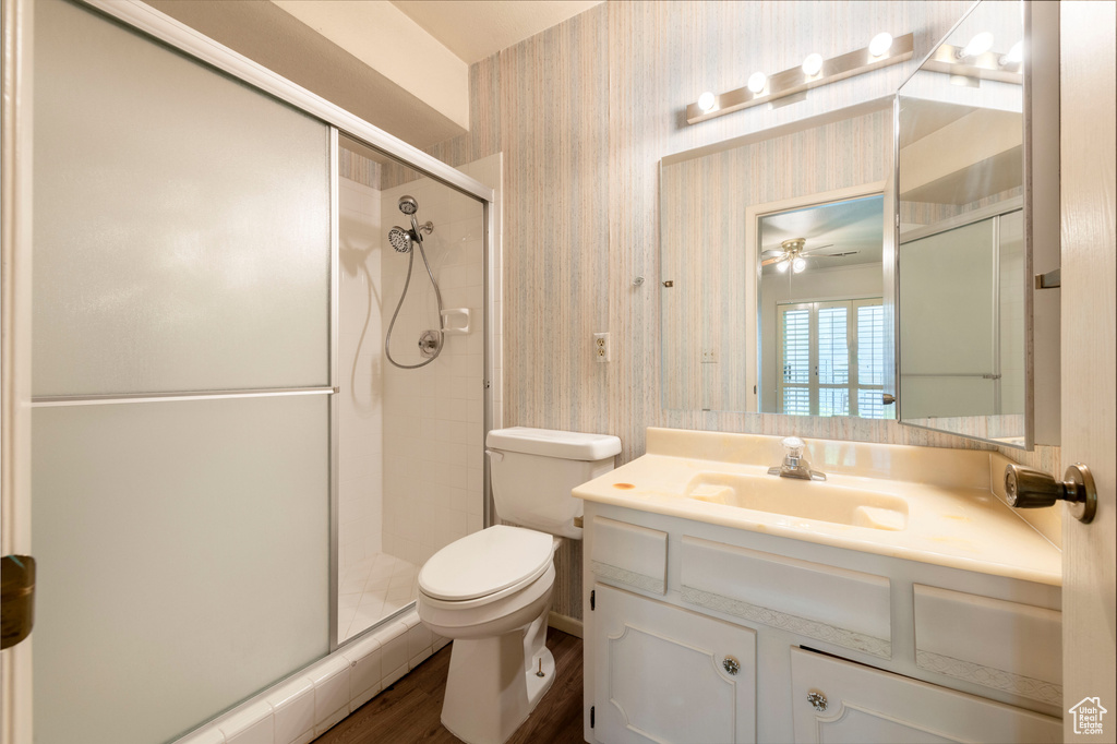 Bathroom with toilet, vanity, a stall shower, wood finished floors, and wallpapered walls