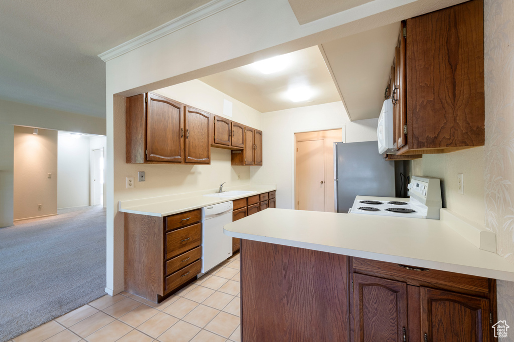 Kitchen with white appliances, a peninsula, light countertops, light tile patterned floors, and light carpet