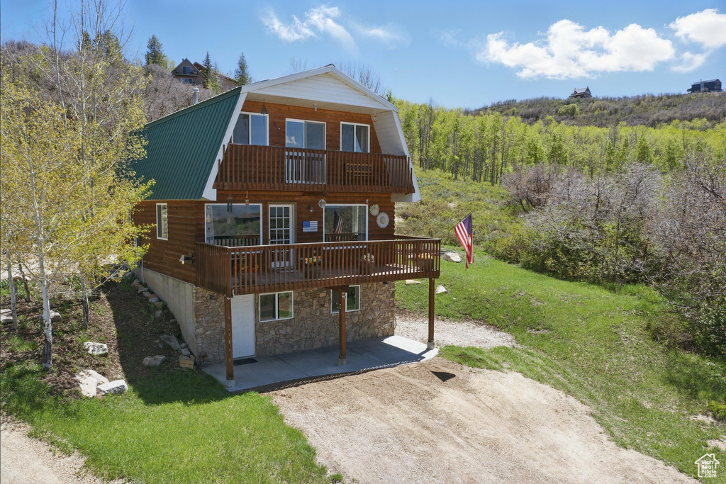 Back of property featuring a patio area, a gambrel roof, a yard, stone siding, and metal roof