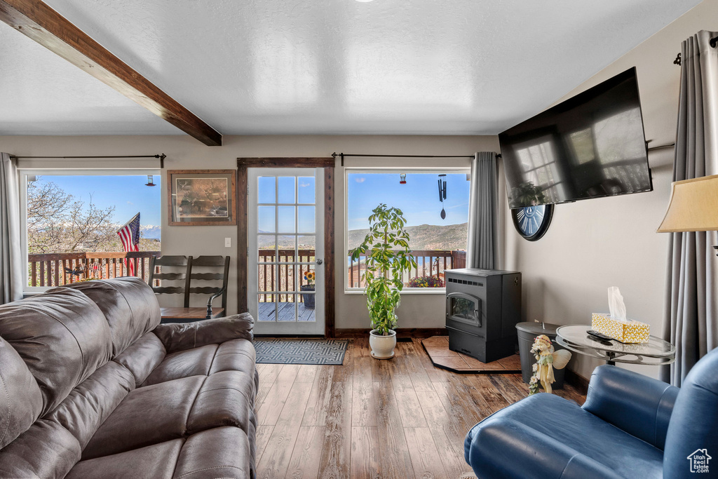 Living area featuring a wood stove, beam ceiling, wood-type flooring, and baseboards