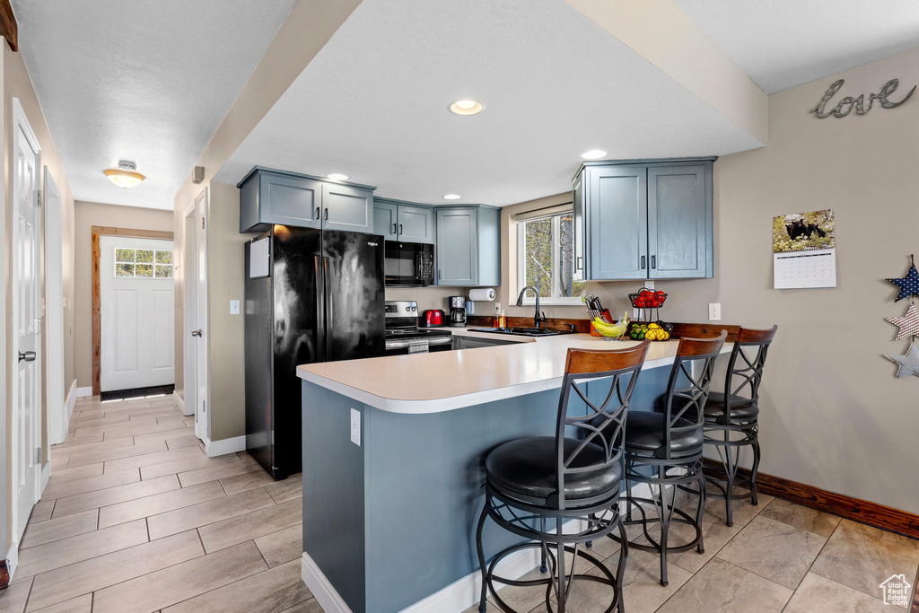 Kitchen with black appliances, a peninsula, baseboards, a sink, and a kitchen breakfast bar