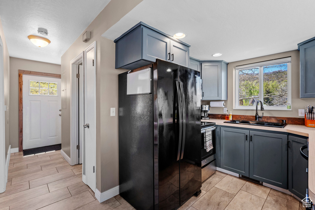 Kitchen with freestanding refrigerator, a sink, baseboards, light countertops, and gray cabinets