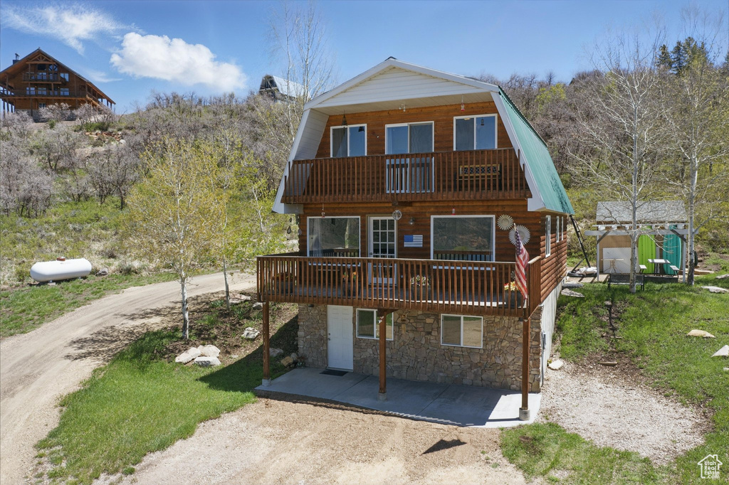 View of front facade with a balcony, a gambrel roof, stone siding, and a wooden deck
