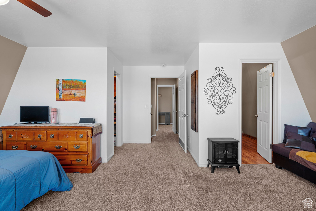 Bedroom with light colored carpet, baseboards, ceiling fan, and a wood stove