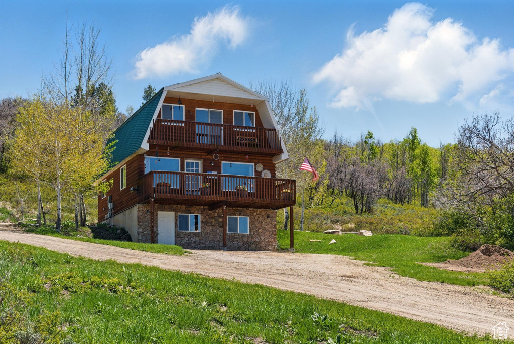 Back of house featuring a gambrel roof, stone siding, driveway, metal roof, and a deck